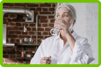 Photo of woman drinking a glass of water in the kitchen.